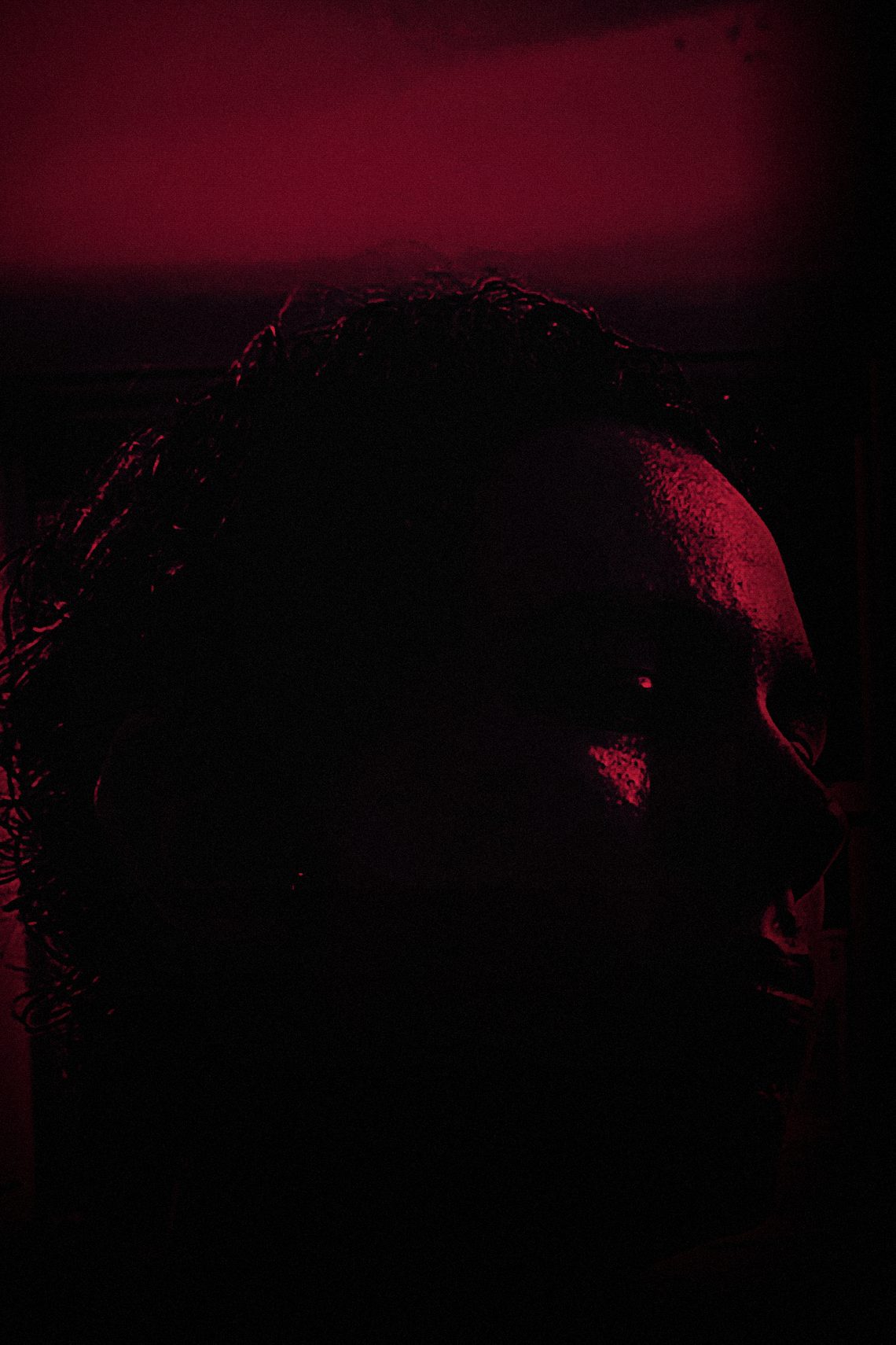 Yiğit Pursalı in profile, almost entirely in shadow with a thin crimson rim of light